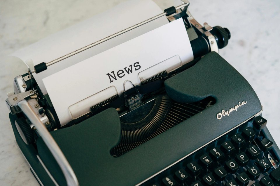 Close-up of a vintage Olympia typewriter with a sheet of paper reading "News" inserted, showcasing the classic design and keys.